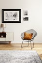 Orange pillow on a black, industrial net chair by a white wall with gallery of mock-up pictures in an elegant living room interior