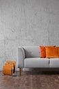 Orange pillows on grey settee in living room interior with concrete wall and wooden floor. Real photo Royalty Free Stock Photo