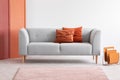 Orange pillows on grey sofa in grey living room interior. Real photo