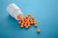 orange pills fall out of a plastic bottle on a blue background Royalty Free Stock Photo