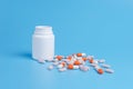 Orange and pink pills, tablets and white bottle on blue background Royalty Free Stock Photo
