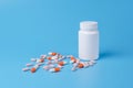 Orange and pink pills, tablets and white bottle on blue background Royalty Free Stock Photo