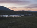 Orange pink sunset at wild water of Vuojatadno river rapids, mountain and birch tree forest. Beatiful northern artic