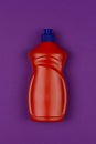 Orange plastic bottle of dishwashing liquid on purple background close-up