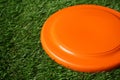 Orange plastic frisbee disk on green grass, closeup