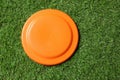 Orange plastic frisbee disk on green grass, top view