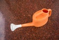 Orange plastic watering can on granito tile floor Royalty Free Stock Photo