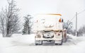 Orange plough truck on snow covered road; gray sky and trees in background; view from car driving behind - winter road maintenance Royalty Free Stock Photo