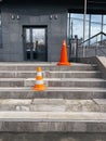 Orange protective cones on broken steps at entrance to office building warn of danger.