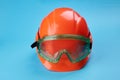 Orange protective helmet and safety glasses near it on a bright blue background. protective workwear and construction Royalty Free Stock Photo