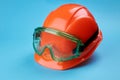 Orange protective helmet and safety glasses near it on a bright blue background. protective workwear and construction Royalty Free Stock Photo