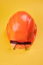 Orange protective helmet and safety glasses near it on a bright yellow background. vertical orientation. protective Royalty Free Stock Photo