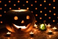 Orange pumpkin as a head with carved eyes and a smile with candles on a black background with a garland to the Halloween party Royalty Free Stock Photo