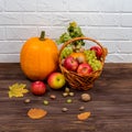 Orange pumpkins with apples and pears in a wicker basket with grapes, nuts and leaves on a brown wooden table against a Royalty Free Stock Photo