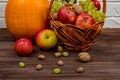 Orange pumpkins with apples and pears in a wicker basket with grapes, nuts and leaves on a brown wooden table against a Royalty Free Stock Photo