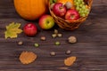 Orange pumpkins with apples and pears in a wicker basket with grapes, nuts and leaves on a brown wooden table against a Royalty Free Stock Photo