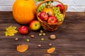 Orange pumpkins with apples and pears in a wicker basket with grapes, nuts and leaves on a brown wooden table against a Royalty Free Stock Photo