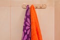 Orange and purple towels hanging on a hanger with hooks in the bathroom. Care and hygiene concept Royalty Free Stock Photo