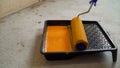 Orange putty and roller in the tray. Putty, tray and roller. Paint roller, tray with orange paint on concrete floor