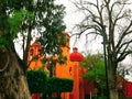 Orange and red historical church in san miguel allende mexico with trees and bushes Royalty Free Stock Photo