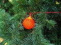 Orange red plastic Christmas light bulb in the form of a ball on a plastic Christmas tree close up. Royalty Free Stock Photo