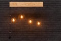 Orange retro lamps hanging on a wooden board on a background of dark black brick wall. Modern template with place for Royalty Free Stock Photo