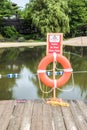 Orange ring buoy and swim at your own risk sign on post near lake
