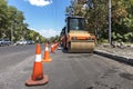 Orange road cones protect heavy wheel compactors along the edge of the city street road