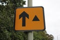 Orange road sign with arrow and black triangle