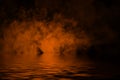 Orange rolling billows of smoke clouds from dry ice across the bottom light with reflection in water