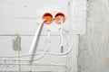 Orange, round junction box mounted in the white wall with protruding electric cables. Royalty Free Stock Photo
