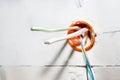 Orange, round junction box mounted in the white wall with protruding electric cables. Royalty Free Stock Photo