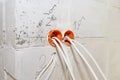 Orange, round junction box mounted in the white wall with protruding electric cables. Royalty Free Stock Photo