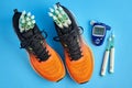 Orange running shoes with insulin syringe pens and a glucometer for measuring blood sugar on a blue
