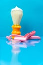 An orange shaving brush at the tip smeared with shaving foam next to pink disposable razors against a light blue background