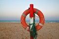 Orange life saver ring with green rope on wooden post. Sandy beach, Corralejo, Fuerteventura at sunrise. Royalty Free Stock Photo