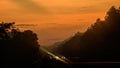 Orange sky and the silhouetted trees in the expressway morning, vehicle headlights