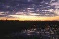 Orange sky sunrise on a dark green wetlands landscape with water reflection and purple clouds