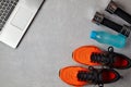 Orange sneakers, dumbbells, a water bottle and a laptop on a gray concrete background