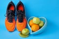Orange sneakers, measuring tape and fruits, apples and oranges in a heart shaped bowl on a blue background Royalty Free Stock Photo