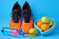 Orange sneakers, measuring tape, water botlle and fruits apples and oranges on a blue background Royalty Free Stock Photo