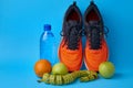 Orange sneakers, measuring tape, water botlle and fruits apples and oranges on a blue background