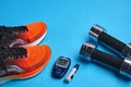 Orange sneakers, metal dumbbells and a blood glucose meter on a blue background