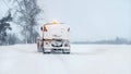 Orange snowplough truck covered with snow, on winter road, gray overcast sky background, view from behind Royalty Free Stock Photo