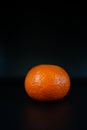 Orange sphere on textured surface, Vivid tangerine resting upon rough dark surface with textured rind Royalty Free Stock Photo