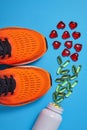 Orange sports sneakers and a jar with poured capsules of polyunsaturated fatty acids and decorative hearts on a blue