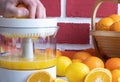 Orange is squeezed on a white juicer, whole oranges on the table