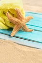 Orange starfish with yellow towel on blue wooden board of pier or sun lounger on sand of beach. Vacation, travel, weekend Royalty Free Stock Photo