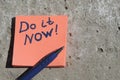 orange sticker with the words do it now and a pen on a concrete surface Royalty Free Stock Photo