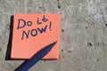 orange sticker with the words do it now and a pen on a concrete surface